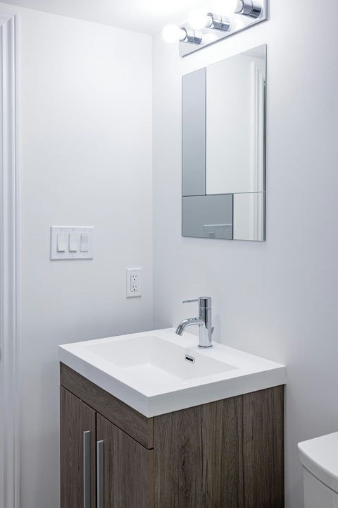small floating wooden vanity with white countertop and faucets