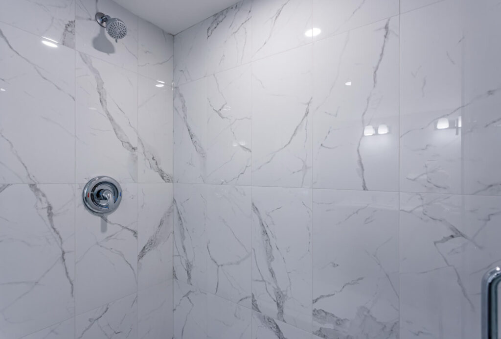 marble tiled shower wall with shower head and controller