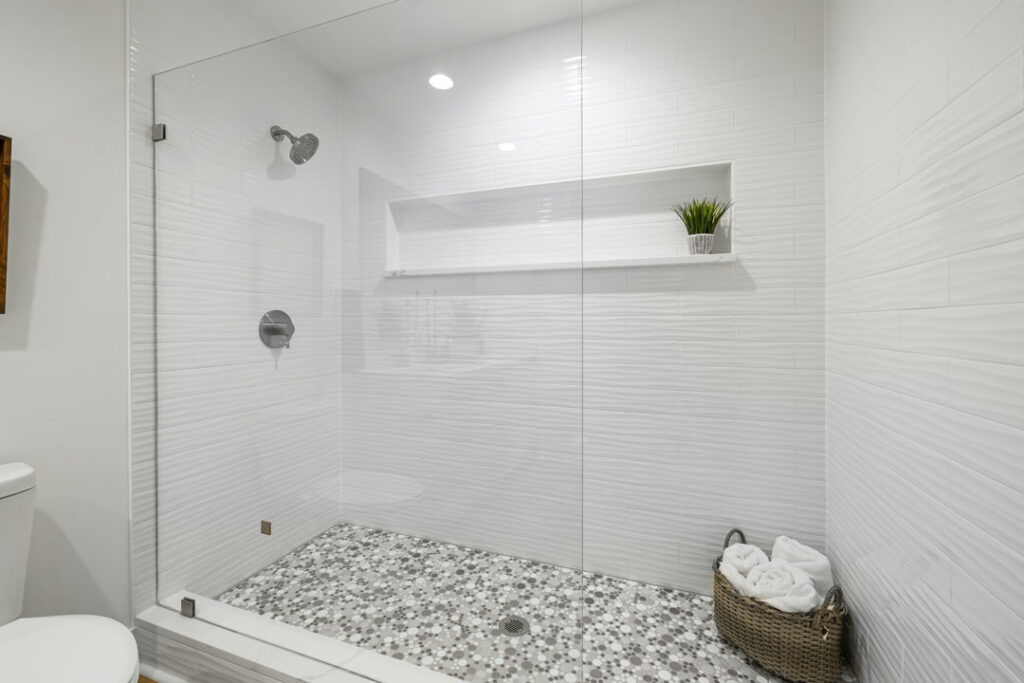 textured white shower tiled walls with mosaic shower flooring and faucets